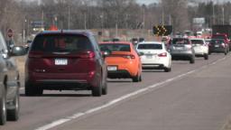 A line of cars driving on the road approaching a merge sign.