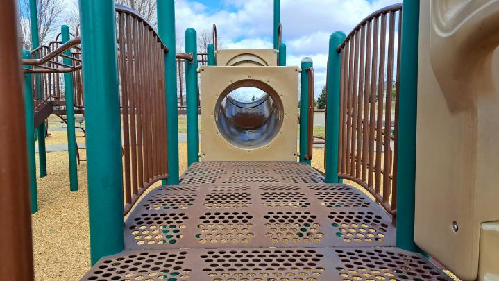 A view of a playground structure with a bridge, railings, and a tunnel.